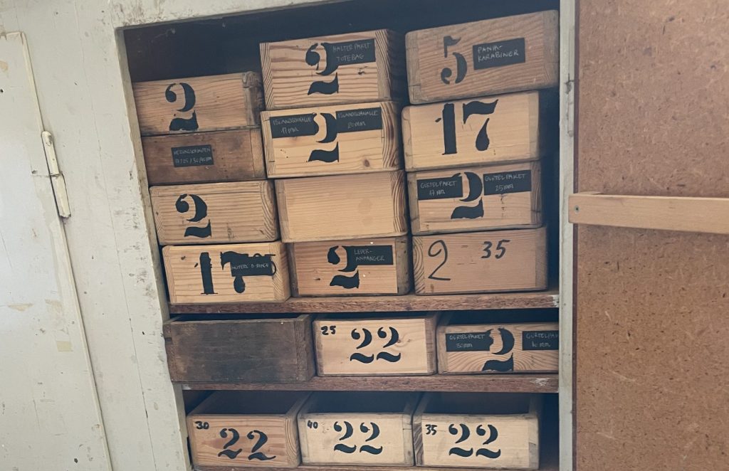 Ein alter Werkzeugschrank mit kleinen Holzkisten. Auf der Vorderseite der Kisten ist in Schablonenschrift jeweils eine Nummer drauf gemalt.